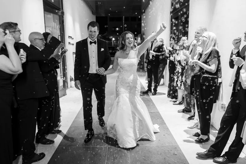 Lauren and Kevin walk hand-in-hand down a confetti-lined aisle flanked by cheering guests in black and white.