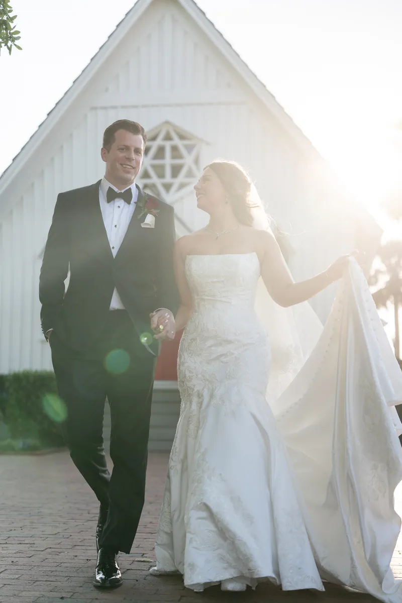 Lauren and Kevin walk away from the chapel as evening light bathes the white structure and surrounding greenery.