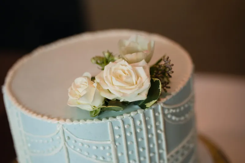 Light blue wedding cake with piped detail and fresh ivory roses and greenery on top.