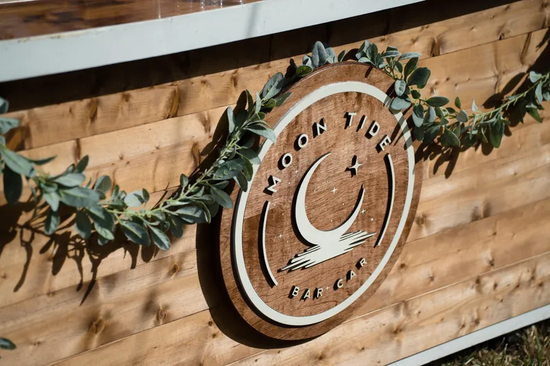 Wooden semicircular sign with metal lettering and eucalyptus garland draped across wooden beam.