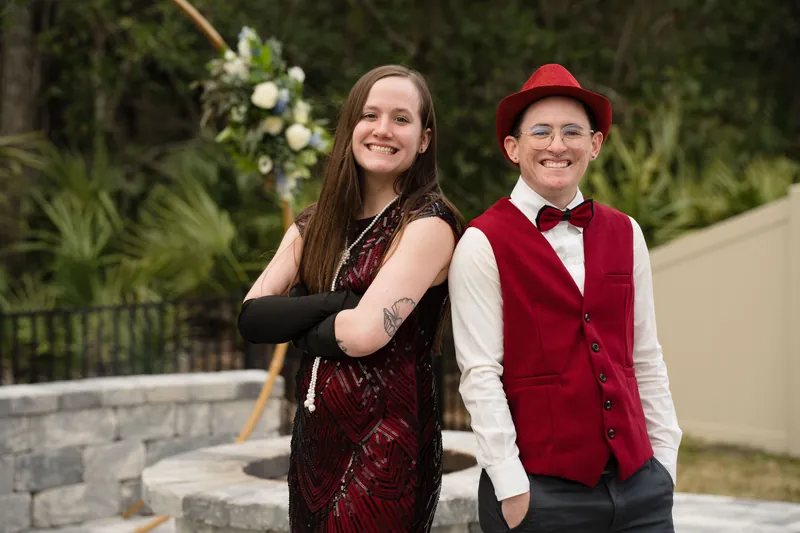 A young woman in burgundy sequins and a child in a red vest and cap smile on an outdoor patio.