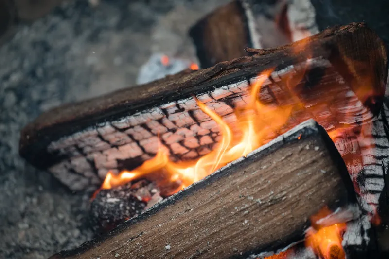Flames and glowing embers consume logs in a close-up of an outdoor fire.