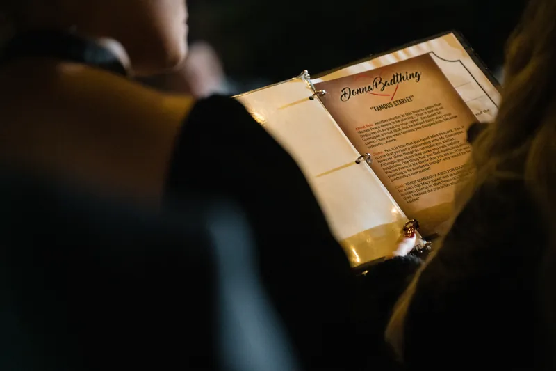 Guests in dark clothing lean over a wooden program during an evening celebration.