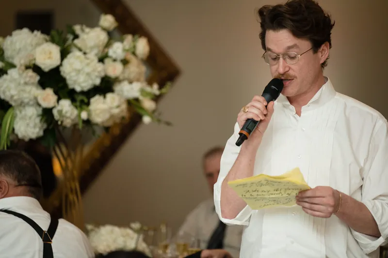 Cole reads from yellow papers into a microphone beside a white floral arrangement during his reception speech.