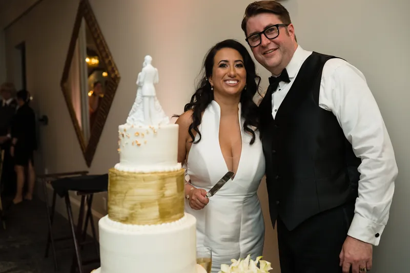 Cole and Lehna stand beside a three-tiered wedding cake with gold leaf details at Casa Monica Resort & Spa.