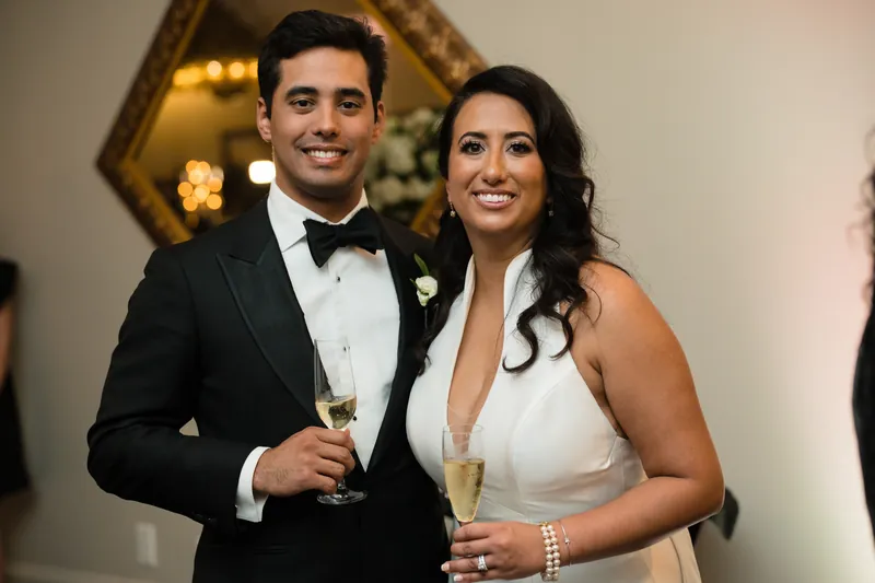Cole and Lehna hold wine glasses and smile at the camera in formal attire.