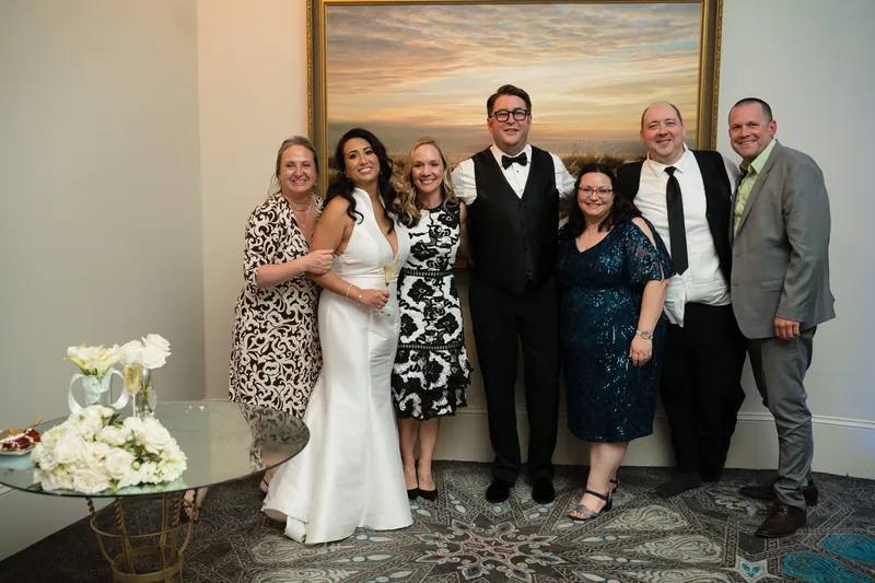Lehna in a white dress stands with six family members for a group portrait indoors.