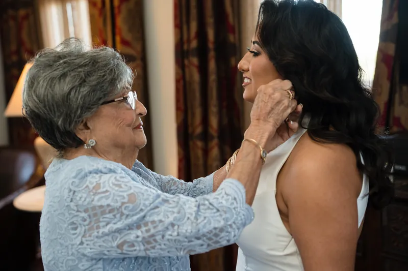 An older woman adjusts Lehna's earring while smiling at the bride before the Cathedral Basilica ceremony.