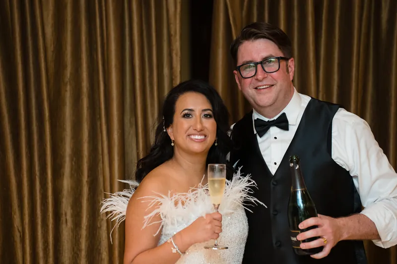 Lehna holds a champagne flute while Cole smiles beside her at Casa Monica Resort & Spa, both dressed formally.