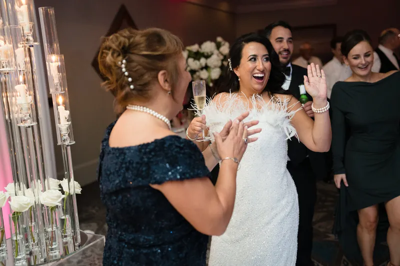 A woman in a sequined navy dress gestures while speaking with Lehna, who wears her white wedding dress.