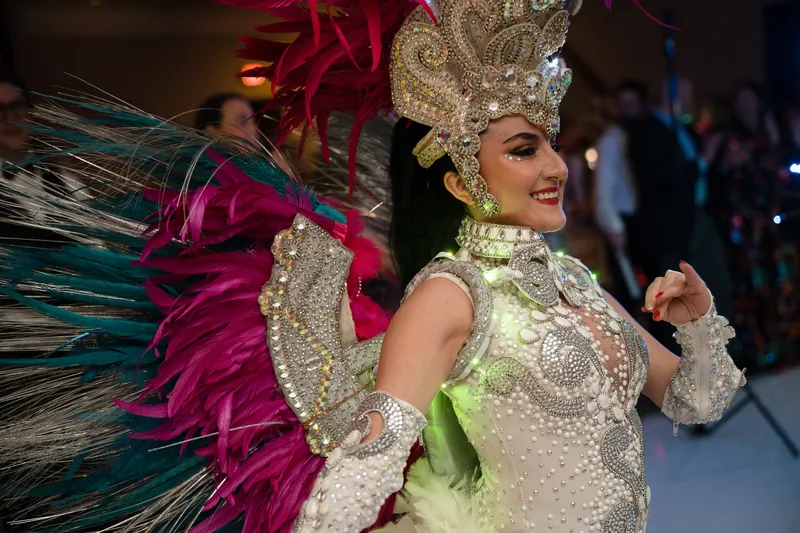 A performer in a shimmering green and white beaded costume with a tall headdress and vibrant feathered wings dances.