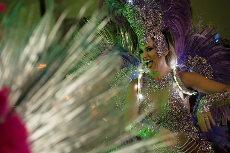 A performer in an ornate sequined costume with colorful feathered wings moves energetically across the dance floor.