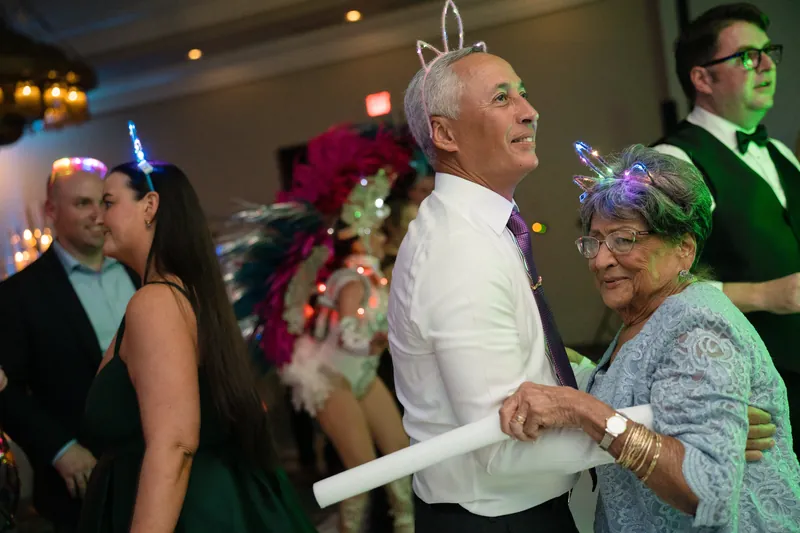 A man in a white shirt dances with an older woman wearing a tiara and feathered headpiece at Casa Monica Resort & Spa.