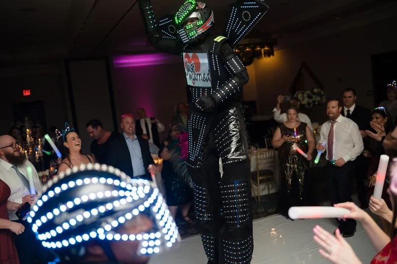 An energetic performer in a black sequined outfit with large feathered wings dances on stage as guests watch and celebrate.