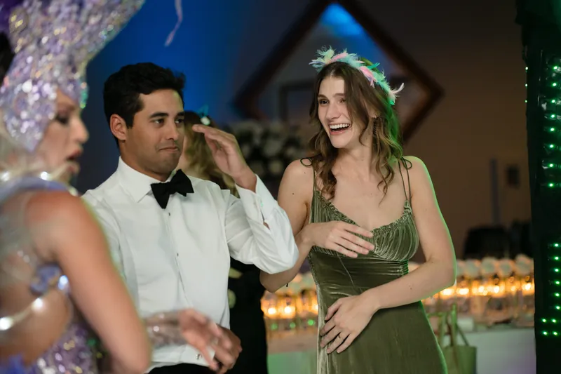 Cole adjusts his bow tie while watching someone in a green dress laugh during the reception's festivities.