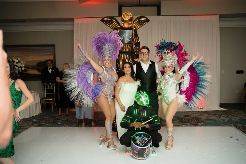 Lehna and Cole pose with four elaborately costumed performers wearing feathered headdresses and shimmering outfits