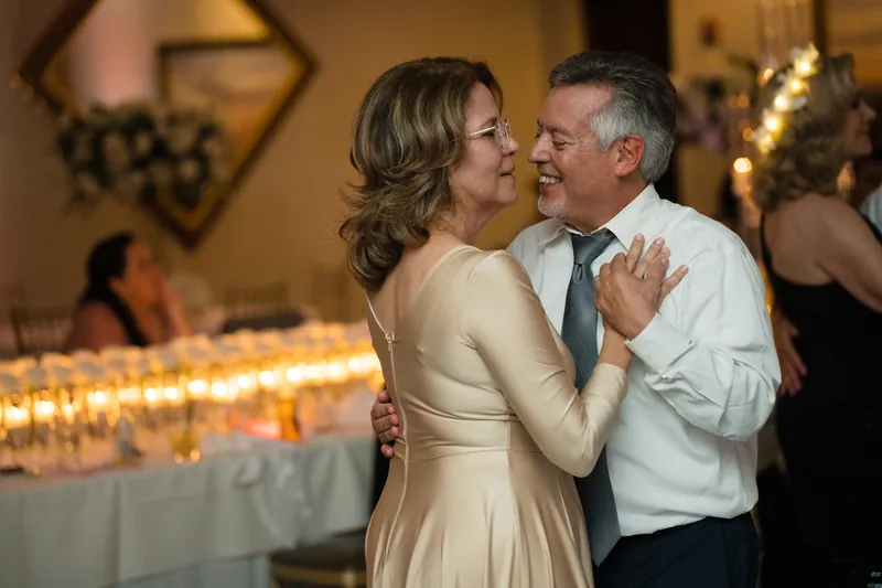 Two guests dance closely together, framed by candlelit tables and warm golden lighting at the venue.