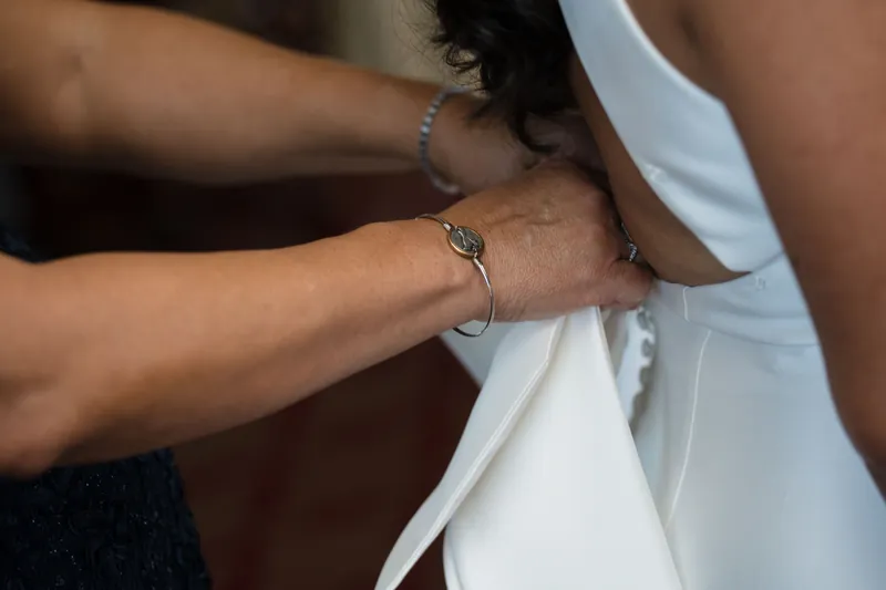Someone adjusts a blue bracelet on Lehna's wrist as she wears her white sleeveless dress.