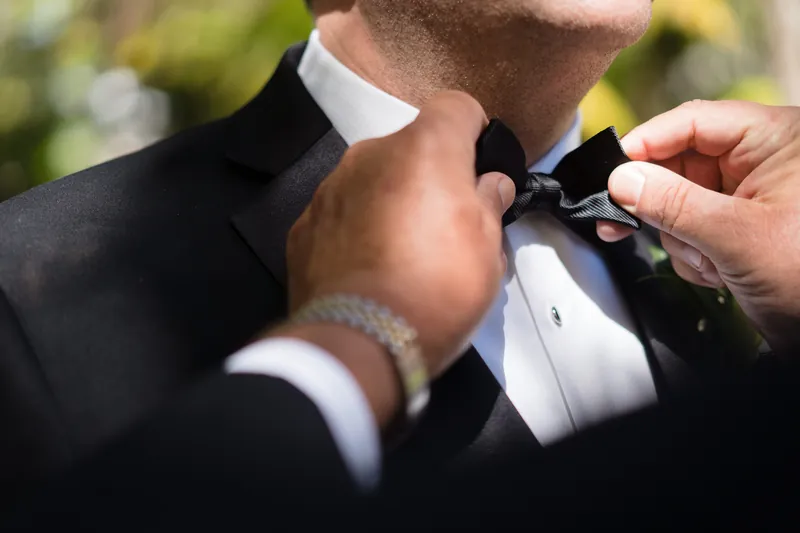 Cole's hands adjust his black bow tie as someone helps him prepare at the Cathedral Basilica of St. Augustine.