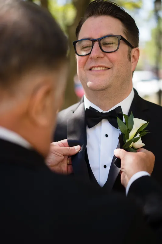 Cole stands in a black tuxedo with a green boutonniere while someone straightens his jacket.