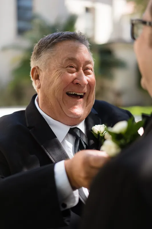 Cole laughs while talking with someone at the Cathedral Basilica of St. Augustine, wearing a dark suit and white boutonniere.