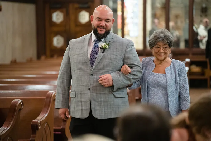 Cole walks down the aisle arm-in-arm with an older woman in a gray cardigan at the Cathedral Basilica.