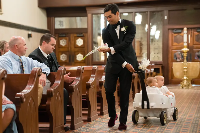Cole guides a small child in a white outfit down the cathedral aisle while guests look on from wooden pews.