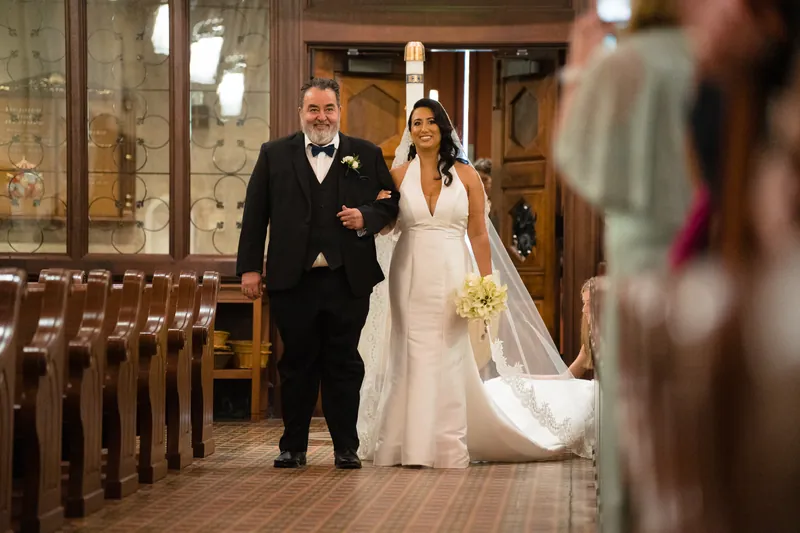 Lehna and Cole walk together down the cathedral aisle, Lehna in a flowing white gown with a long train.
