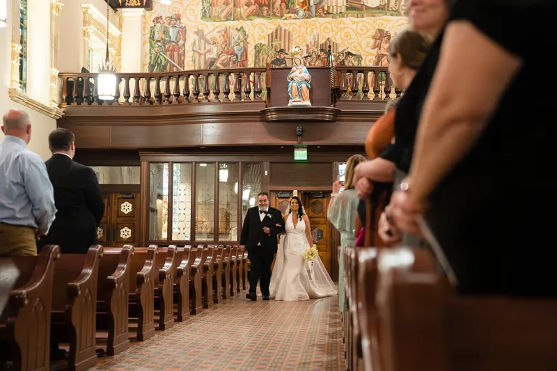 The couple stands together at the altar under ornate basilica architecture as guests watch from the wooden pews.