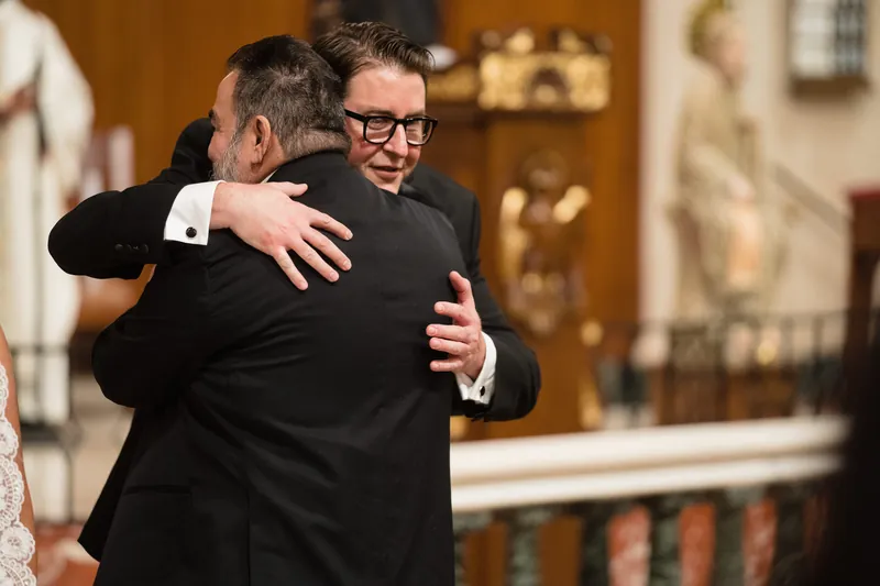 Cole embraces a family member at the Cathedral Basilica of St. Augustine, both wearing formal black attire.