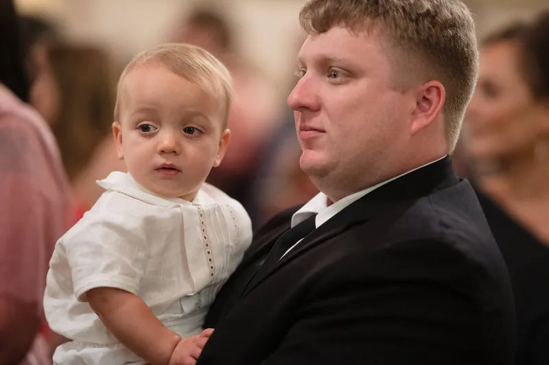 Cole holds a small child in a white outfit during the ceremony at the Cathedral Basilica of St. Augustine.