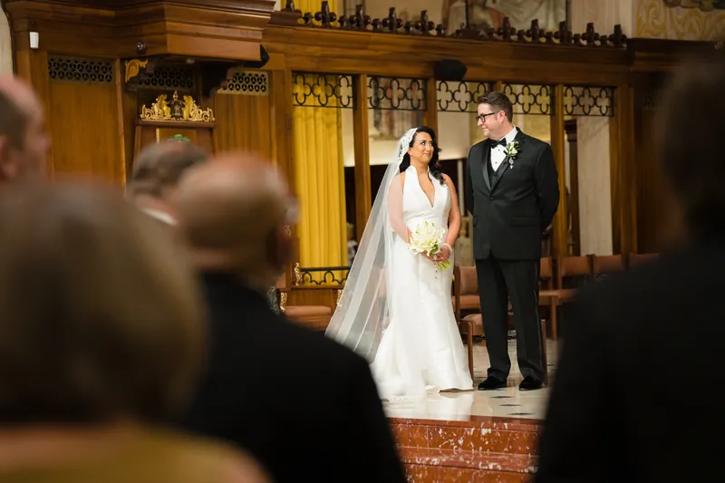 Lehna and Cole stand together at the altar, Lehna in a white gown and veil, Cole in a black tuxedo.