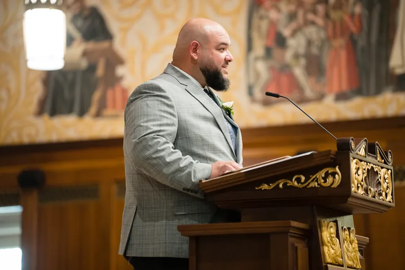 Cole speaks at a wooden lectern with ornate gold details inside the Cathedral Basilica of St. Augustine.