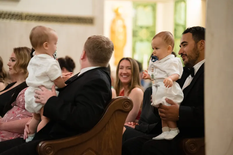 Wedding guests hold young children in formal wear while seated in pews at the Cathedral Basilica of St. Augustine.