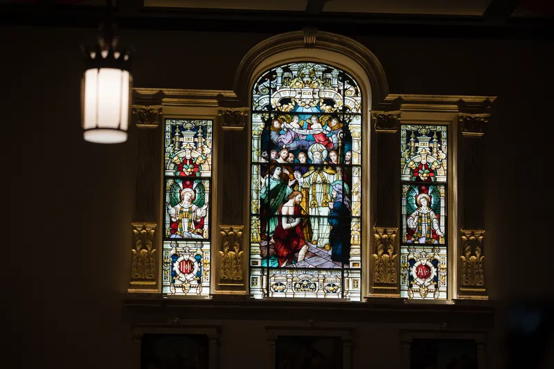 Stained glass window depicting religious figures glows above the basilica's altar area with ornate gold detailing.