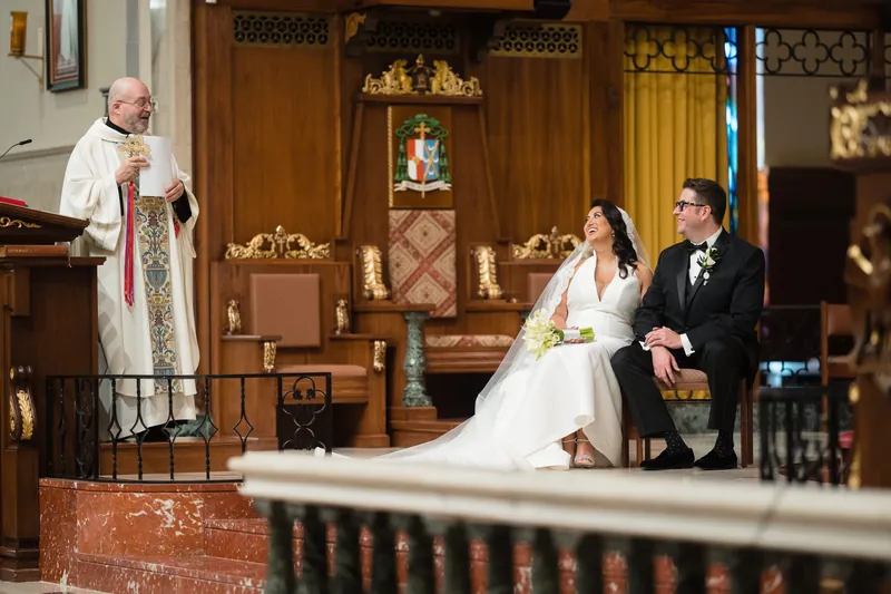 Clergy member leads the couple's vows while Lehna and Cole sit facing forward in the basilica's ornate interior.