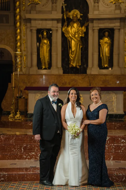 Cole stands between two family members in formal wear, all three smiling in front of the cathedral's gilded religious