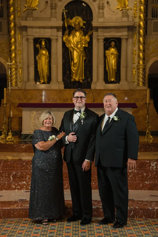 Two family members embrace Cole at the basilica's altar as he beams, with golden religious artwork illuminating the sacred