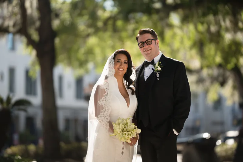 Lehna and Cole stroll side by side beneath mature oak trees at Casa Monica, framed by the historic building's architecture