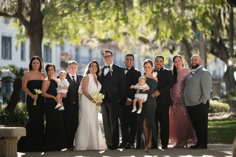Lehna in a white wedding dress stands with Cole and their wedding party beneath oak trees at Casa Monica Resort & Spa, St.