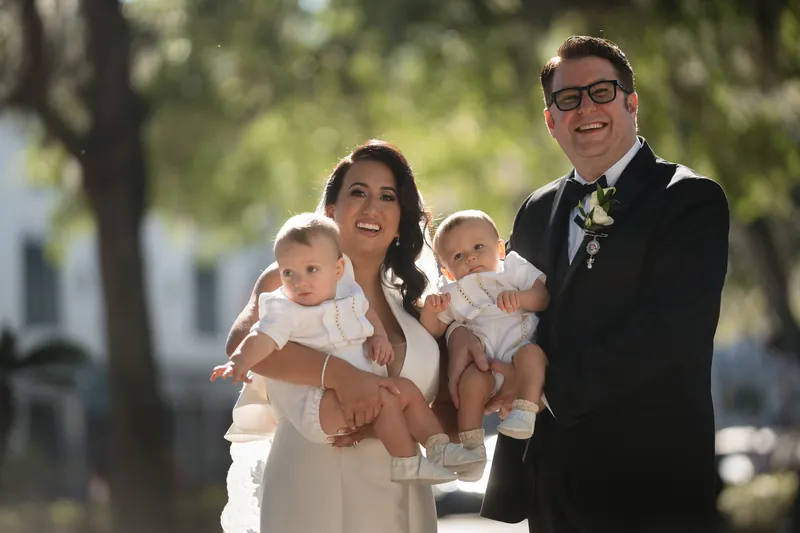 Cole and Lehna hold two infants while posing together under dappled sunlight at Casa Monica Resort & Spa, St. Augustine.