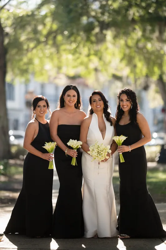 Lehna stands with three attendants in black dresses, each holding yellow and white bouquets at Casa Monica Resort & Spa, St.