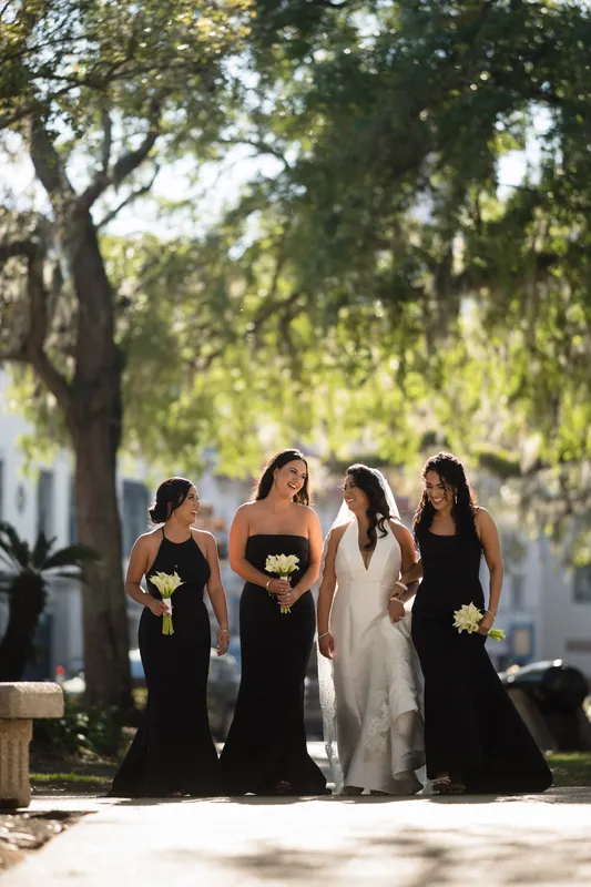Four women in black gowns and Lehna in white walk together under tree-lined grounds at Casa Monica Resort & Spa, St.