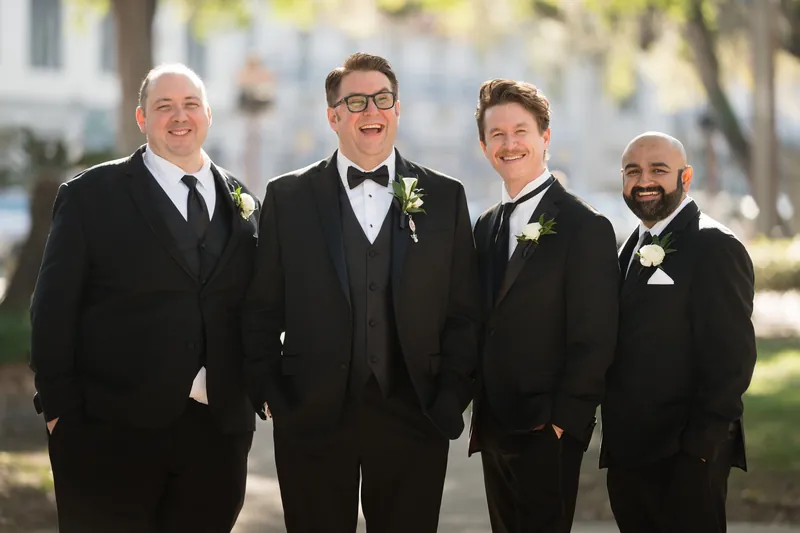 Cole stands with three groomsmen in black tuxedos, all wearing boutonnieres, at Casa Monica Resort & Spa, St. Augustine.