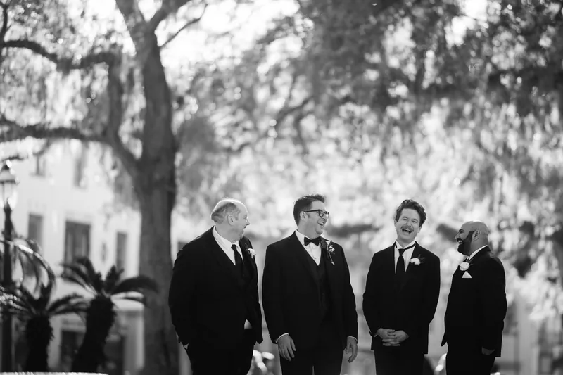 Four men in black formal wear walk together beneath Spanish moss-draped trees at Casa Monica Resort & Spa, St. Augustine.