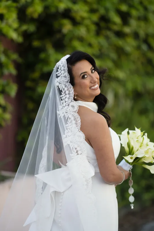 Lehna looks over her shoulder in a white lace wedding dress and veil against greenery at Casa Monica Resort & Spa.