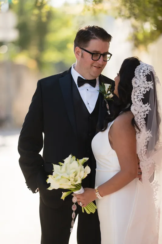 Cole and Lehna walk down a tree-lined brick path, sunlight filtering through the leaves as they stroll together.