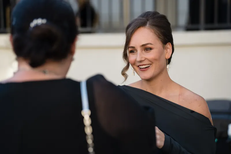 A woman in a black off-shoulder dress smiles while facing away from the camera.