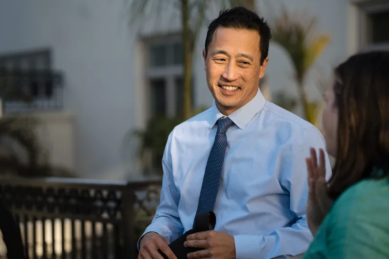 A man in a light blue shirt and tie chats with a guest at the reception.