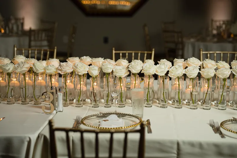 White roses in tall glass vases line the banquet table at Casa Monica Resort & Spa, with gold-rimmed place settings visible